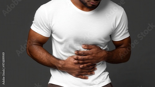 A man in a white shirt experiencing stomach discomfort, capturing a moment of pain and unease against a dark background.