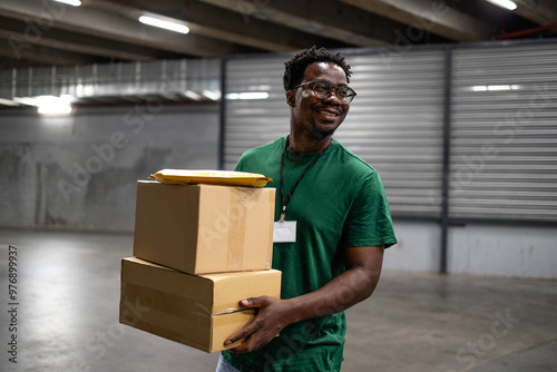 Smiling black delivery man sorting parcels inside warehouse. photo