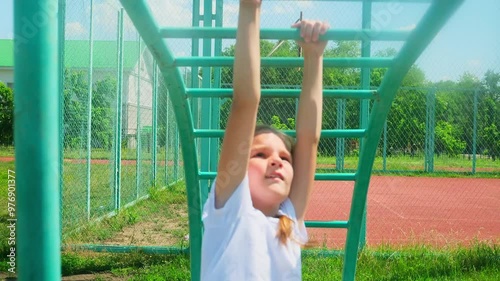 Strong cute 8 year old girl exercising on monkey bars outdoor on sport ground. Slow motion, 4K photo