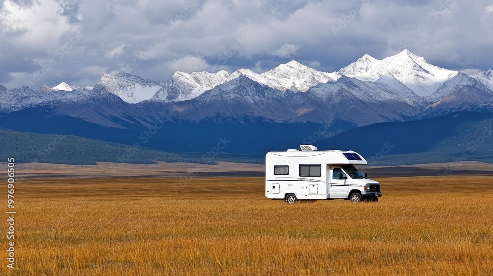A white RV with solar panels rests in golden grassland, surrounded by majestic snow-capped mountains and under a dramatic cloudy sky, perfect for outdoor living. A white RV with solar panels rests in golden grassland, surrounded by majestic snow-capped mountains and under a dramatic cloudy sky, perfect for outdoor living.