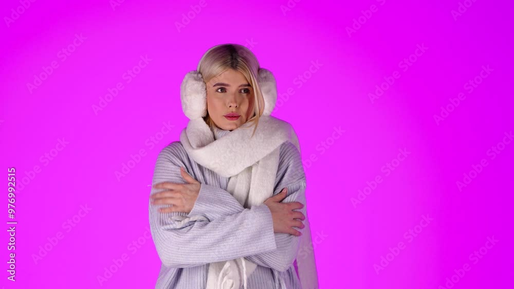 Portrait Of Young Blonde Woman Feeling Cold, Wearing Scarf Grey Sweater and Earmuffs, Studio Shot With Pink Background Portrait Of Young Blonde Woman Feeling Cold, Wearing Scarf Grey Sweater and Earmuffs, Studio Shot With Pink Background