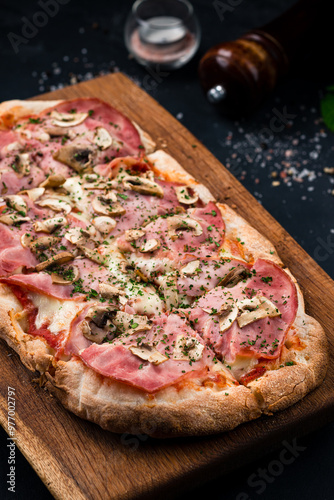Italian cuisine pizza with ham, mushrooms, cheese, tomato sauce and greens on a wooden board.