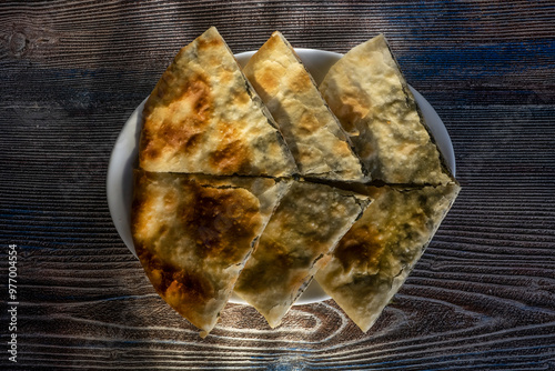 Pie with spinach, herbs and Suluguni cheese on a wooden board. The whole cake with the piece cut off.