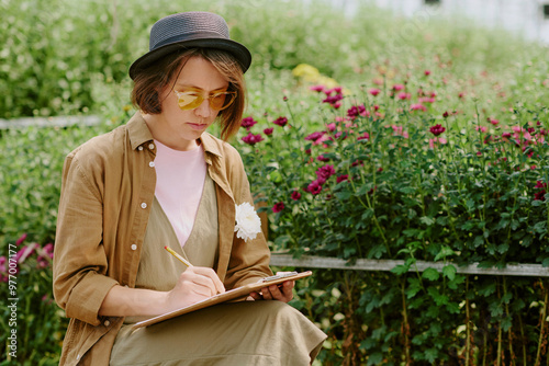 Behang Person sitting in garden and sketching in notebook while surrounded by vibrant flowers