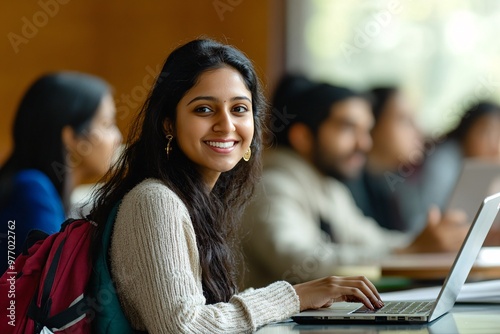 A young woman smiles while studying in a modern classroom, showcasing determination and engagement with her laptop.