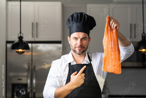 A chef is holding a piece of salmon in his hand and wearing a black hat. High quality photoA chef is holding a piece of salmon in his hand and wearing a black hat. Concept expertise in the kitchen photo