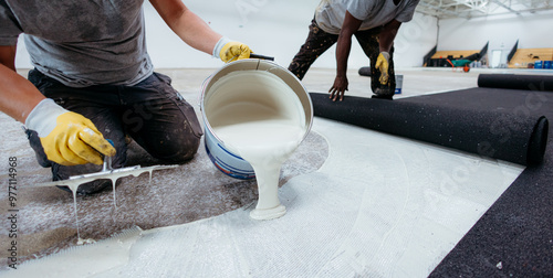 Schilderij op canvas Construction workers pouring glue and laying down flooring in warehouse