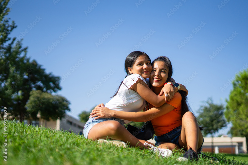Two Latina sisters hugging in a park, one a teenager and one a young adult Two Latina sisters hugging in a park, one a teenager and one a young adult