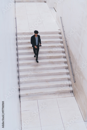 Aerial top of millennial hipster guy with modern digital tablet in hand at urban setting, trendy dressed young man with touch pad in hands going down at city stairs during travel destination