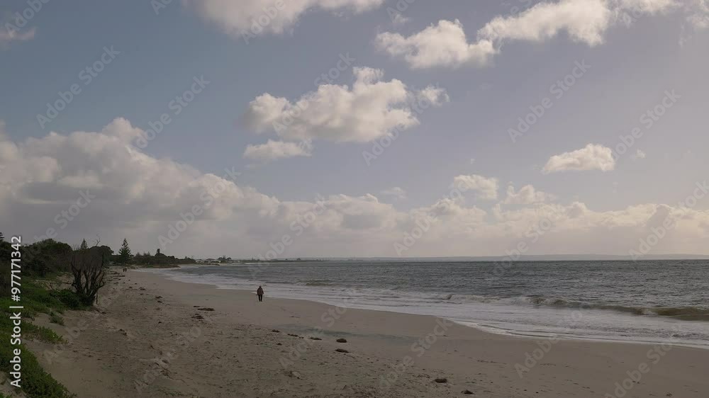 Swirling cumulous clouds sweep over waters of Indian Ocean. Patches of sun shine through with walkers and their dogs zipping up sandy beach. Edges of dunes visible Swirling cumulous clouds sweep over waters of Indian Ocean. Patches of sun shine through with walkers and their dogs zipping up sandy beach. Edges of dunes visible