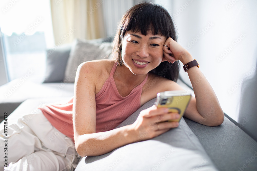 Woman smiling while using smartphone with earbuds in on home sofa