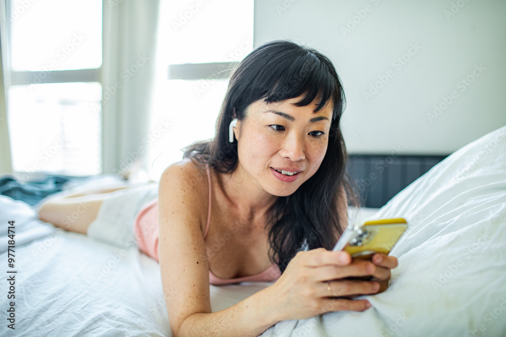 Smiling Asian woman using smartphone in bed at home Smiling Asian woman using smartphone in bed at home