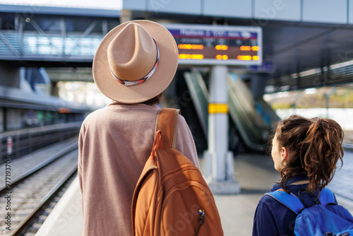 Mom and child with backpacks are waiting for the train on the platform. The family is ready to travel. We are going on vacation with small children.