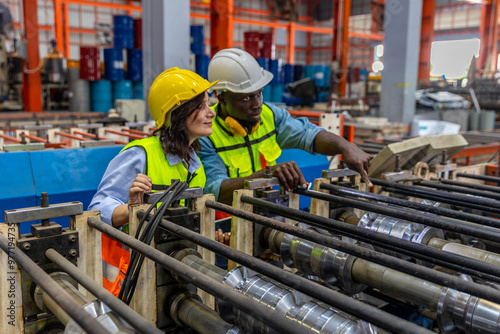 Female mechanical engineer is coaching and providing support to her trainee while examining the functions of metal machines in a factory. Teamwork between two engineers in a factory production plant