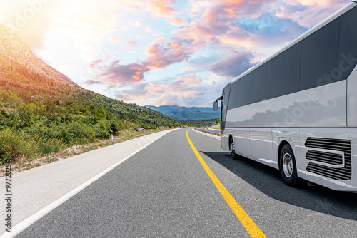 A white tourist bus travels along a picturesque mountain road.