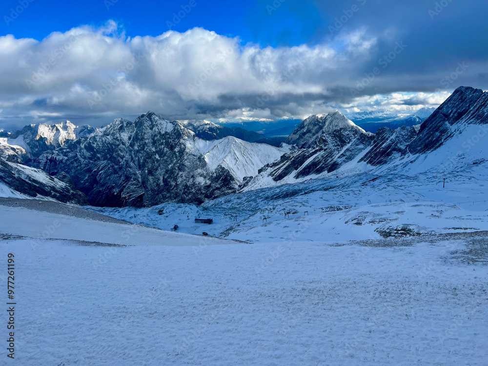 Naklejka premium A stunning view of snow-covered mountain ranges and valleys seen from the top of Zugspitze in Germany. The vast alpine landscape stretches out in a breathtaking winter scene.