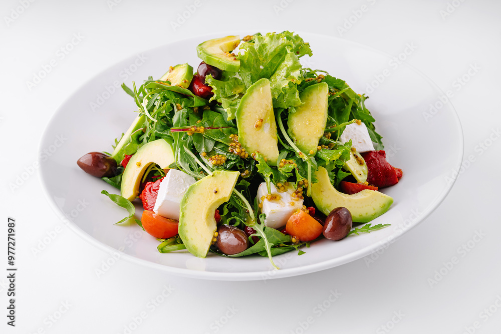 Fresh salad with avocado, feta cheese and olives served on white plate Fresh salad with avocado, feta cheese and olives served on white plate