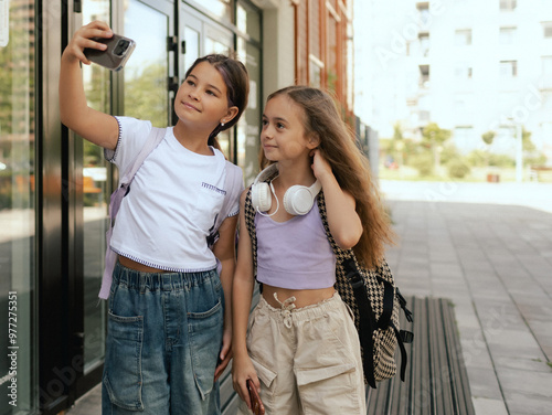 Multiethnic elementary middle school. Girls classmates with backpack in casual clothes take a selfie in the school yard. Gen Alpha. Part of a series.