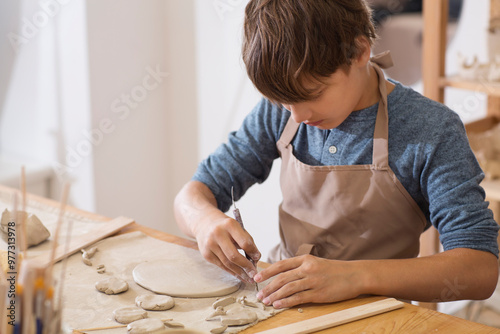 teenager boy works with clay makes  ceramic plate in pottery school.  Children arts a crafts class in workshop. child sculpts from clay