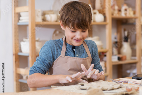teenager boy works with clay makes  ceramic plate in pottery school.  Children arts a crafts class in workshop. child sculpts from clay