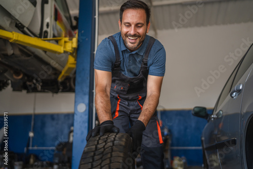 Happy adult man car mechanic work and pushes car tire in auto garage