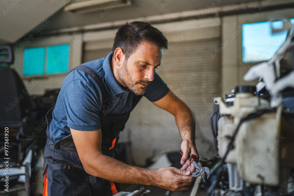 Car mechanic working on a car engine in a workshop with tools visible Car mechanic working on a car engine in a workshop with tools visible