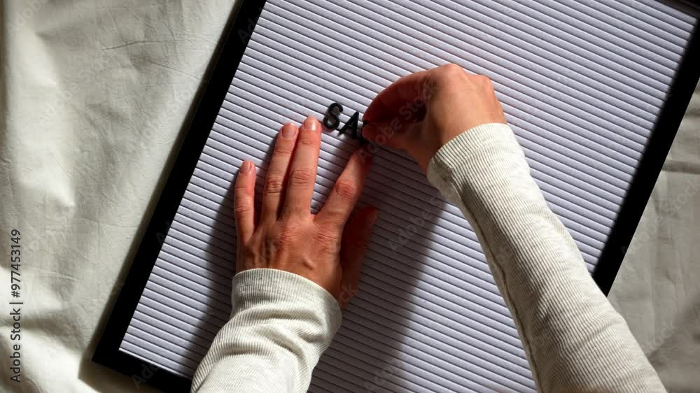 Woman composes the message save the date on a white letter board using her hands. The scene captures the creativity and personal touch involved in crafting a wedding announcement