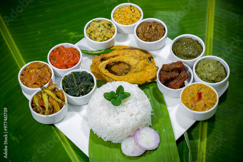 Traditional Bengali dishes such as bhorta, bhaji, fish curry, and vegetable curry are served in white ceramic pots and with Banana leaves. photo