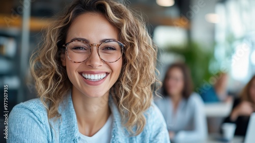 A cheerful woman with glasses beams in a vibrant office space, exuding enthusiasm and optimism, signaling productivity and teamwork within a creative environment.