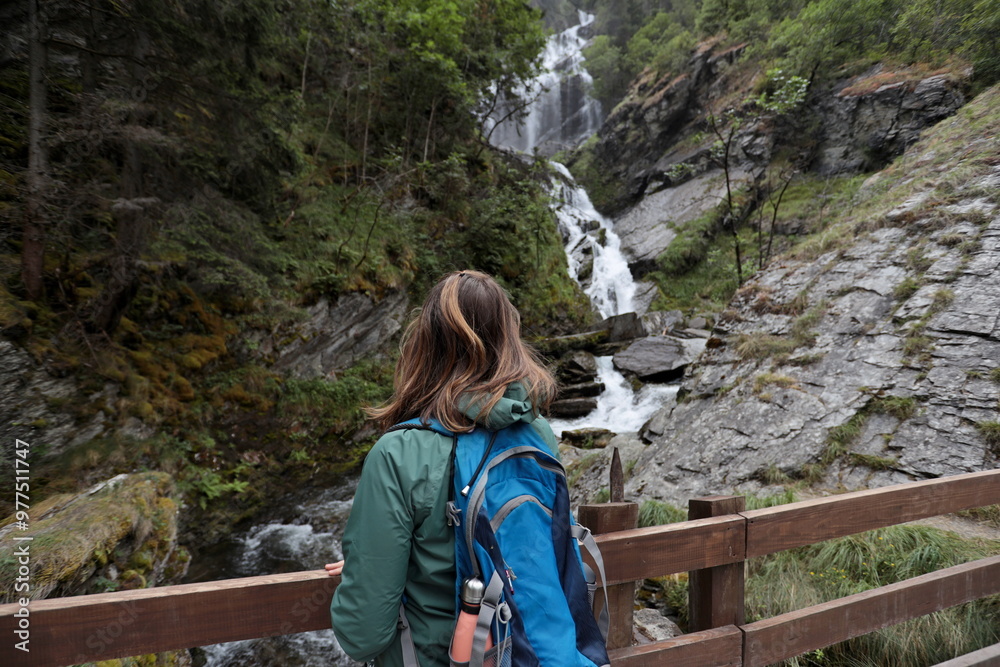 Naklejka premium Girl from behind admires the Lenteney Waterfall in La Salle in Aosta Valley, Italy.