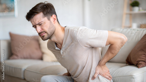 Man with back pain sitting on couch and holding lower back at home