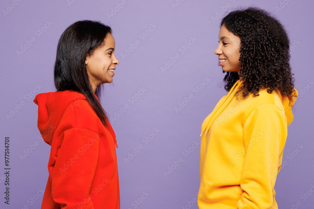 Side profile view two smiling fun young little kid teen girls women they wear red yellow hoodie casual clothes looking to each other isolated on plain pastel light purple background Lifestyle concept Side profile view two smiling fun young little kid teen girls women they wear red yellow hoodie casual clothes looking to each other isolated on plain pastel light purple background Lifestyle concept