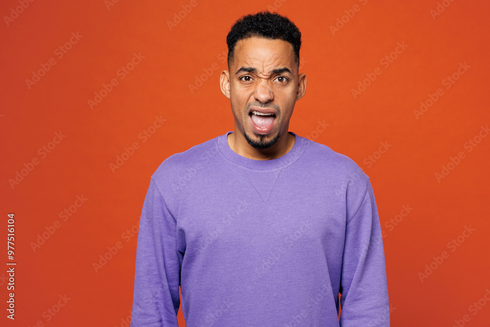 Young sad mad dissatisfied man of African American ethnicity wear purple sweatshirt casual clothes look camera shout scream isolated on plain red orange background studio portrait. Lifestyle concept. Young sad mad dissatisfied man of African American ethnicity wear purple sweatshirt casual clothes look camera shout scream isolated on plain red orange background studio portrait. Lifestyle concept.