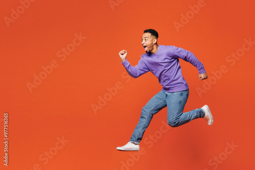 Full body young happy man of African American ethnicity wears purple sweatshirt casual clothes jump high run fast hurry up isolated on plain red orange background studio portrait. Lifestyle concept.