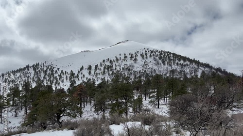 The beautiful snow-capped cinder cone volcano in Sunset Crater National Monument in Arizona, USA. Clouds loom in the sky on this cold winter's day. photo