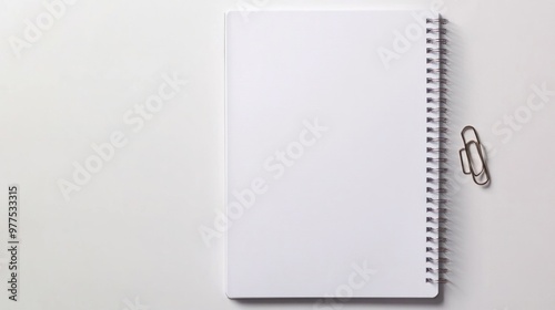 A blank notebook page with a paper clip attached, placed neatly on a smooth white table, ideal for office or study purposes.