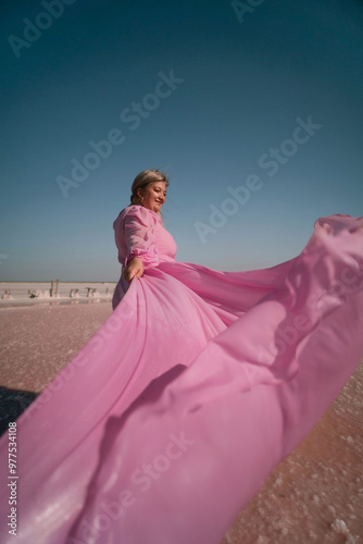 Obraz na plátně Woman Pink Dress Salt Lake - A woman in a pink dress stands on a pink salt lake with the wind blowing her dress
