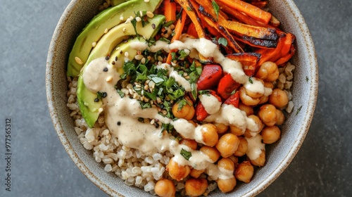 A top view of a vegan Buddha bowl with brown rice, roasted vegetables, avocado, chickpeas, and a tahini dressing drizzle.