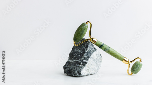 Green jade roller massager for face on white marble.