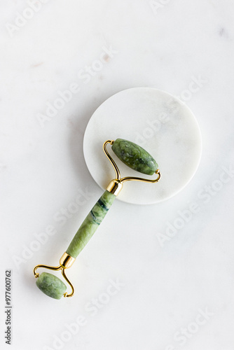 Green jade roller massager for face on white marble.