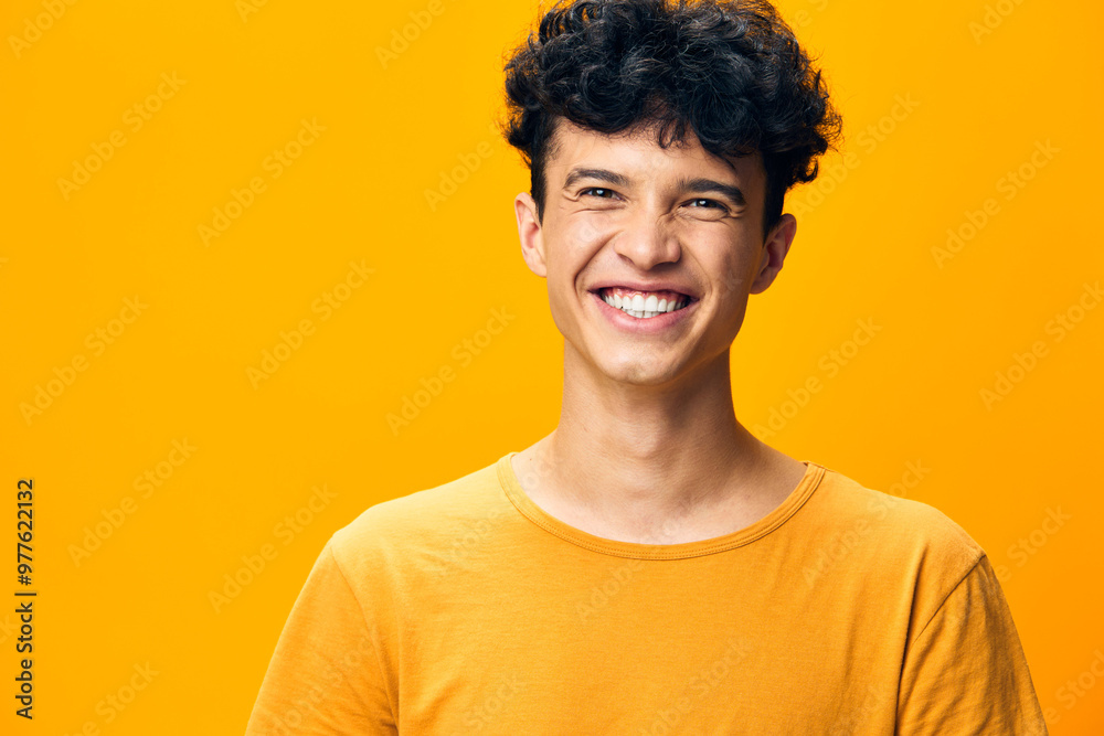 Smiling young man with curly hair in a bright yellow t shirt against a vibrant yellow background exuding happiness and positivity The image captures joy and energy perfectly Smiling young man with curly hair in a bright yellow t shirt against a vibrant yellow background exuding happiness and positivity The image captures joy and energy perfectly