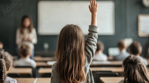 A girls hand raised in a classroom from the perspective of the student behind her emphasizing the moment of eager participation photo