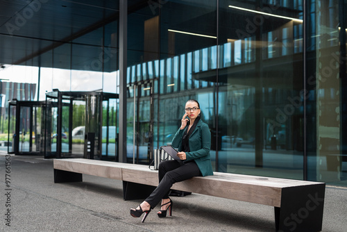 pretty caucasian businesswoman is walking and talking by phone near modern office building