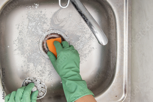A man in green gloves cleans the sink and sink drain with cleaning powder. Top view photo