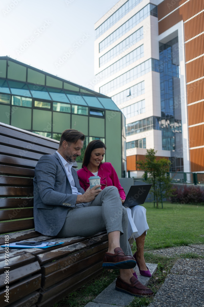 Team of diverse partners sitting at bench mature Latin business man and European business woman discussing project on laptop at park. Two colleagues of professional business people working together. Team of diverse partners sitting at bench mature Latin business man and European business woman discussing project on laptop at park. Two colleagues of professional business people working together.