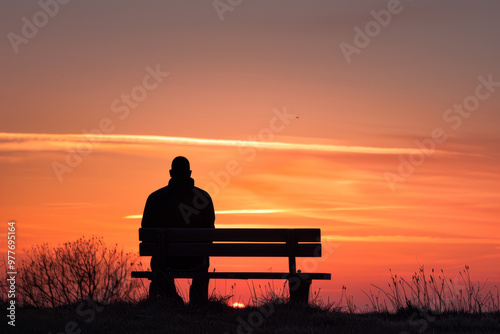 A man sits on a bench in the evening, watching the sun set