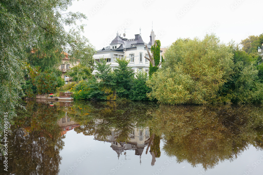 Lush greenery and riverside villa in city park with tall trees and reflections in the Svartan River. Relaxation and urban escape concept. Orebro, Sweden. Space for text Lush greenery and riverside villa in city park with tall trees and reflections in the Svartan River. Relaxation and urban escape concept. Orebro, Sweden. Space for text