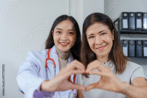 Young doctor and her senior patient are making a heart shape with their hands, expressing care and empathy during a medical consultation photo