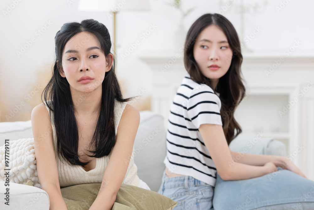 Two angry female friends sitting separately on sofa after having a big fight Two angry female friends sitting separately on sofa after having a big fight
