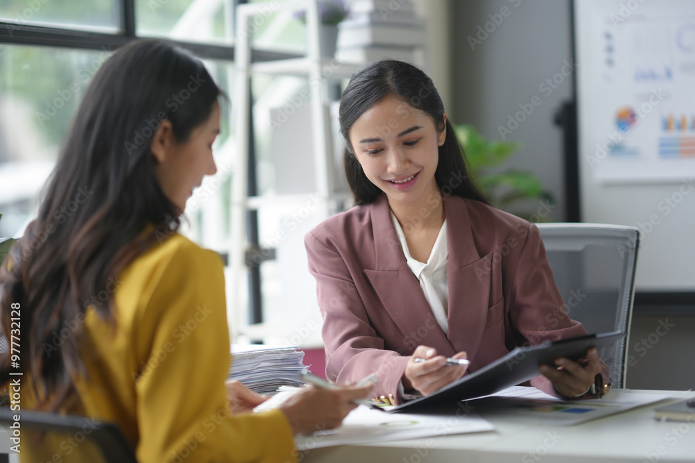 Two businesswomen collaborate in an office, reviewing financial reports and discussing strategies Two businesswomen collaborate in an office, reviewing financial reports and discussing strategies